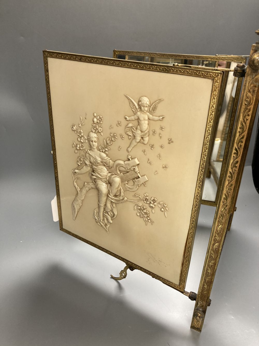 A gilt framed triptych mirror with faux ivory angelic panel and similar floral painted panel, height 41cm